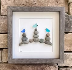 three little birds sitting on top of rocks in front of a stone wall with a wooden frame