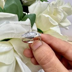 a person is holding a diamond ring in their left hand and white flowers behind them