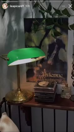 a green lamp sitting on top of a wooden table next to a painting and books