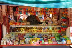 a woman standing in front of a food stand filled with lots of different types of foods