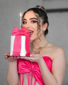 a woman in a pink dress holding a cake with a lit candle on top of it