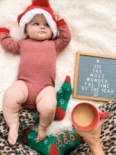 a baby wearing a santa hat laying on top of a leopard print blanket next to a cup of coffee