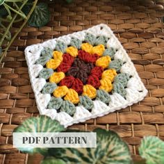 a crocheted square with yellow, red and green flowers on it sitting next to a potted plant