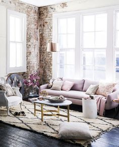 a living room filled with furniture and pillows next to a brick wall covered in flowers