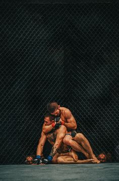 two men wrestling in front of a chain link fence with their arms around each other