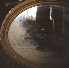 the reflection of a person in a round mirror on a wooden floor with other objects behind it