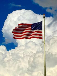 an american flag flying high in the sky on a cloudy day with blue skies and white clouds