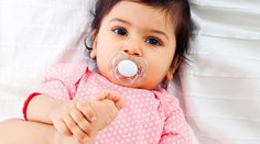 a baby with a pacifier in her mouth laying on a bed and looking at the camera