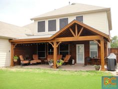 a covered patio with chairs and grill in the back yard, next to a large house