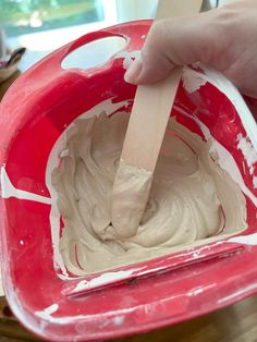 a person is spreading white icing in a red bowl