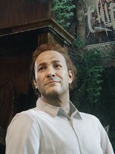 a man standing in front of a building with trees and plants on the wall behind him