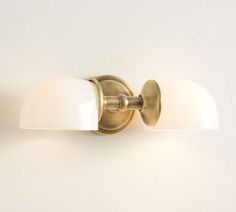 a bathroom light with two white shades on it's side and the wall behind it