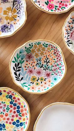 colorful plates with flowers painted on them sitting on a wooden table next to each other