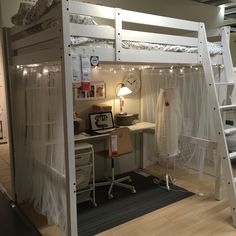 a loft bed with white curtains and lights on the top bunk is next to a desk