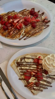 two white plates topped with waffles covered in strawberries and whip cream next to each other