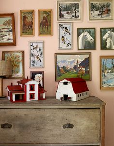 a dresser with many pictures on the wall above it and a toy house sitting on top