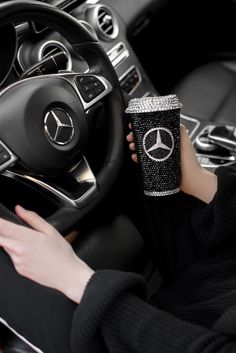 a woman holding a cup in her hand while sitting in the driver's seat of a car