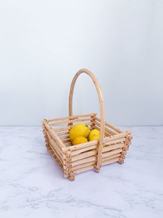 a wooden basket with lemons in it on a marble countertop next to a white wall