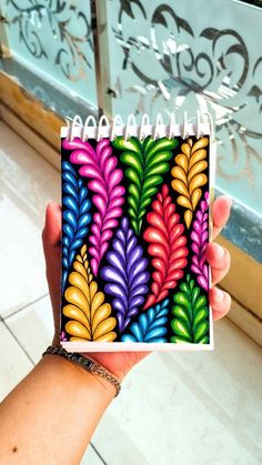 a hand holding up a small notebook with colorful leaves on it