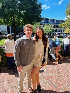 a man and woman standing next to each other on a brick walkway with people in the background