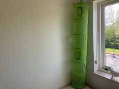 a green curtain hanging from the side of a window next to a white wall and floor