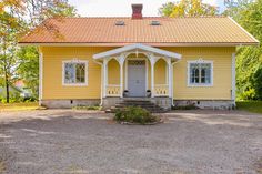 a yellow house with a red roof and white trim on the front door is surrounded by trees