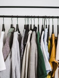 clothes hanging on a rail in front of a white wall and black metal bar holding several different colored shirts