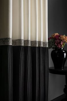 a black vase with flowers in it next to a white and black striped shower curtain