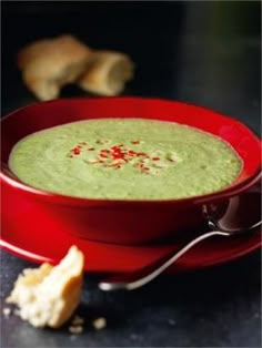 a red bowl filled with green soup next to bread