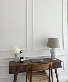 a laptop computer sitting on top of a wooden desk next to a vase with flowers