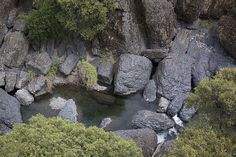 an aerial view of rocks and water in the middle of a forest with trees on either side