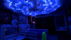 a bed room with a blue sky filled with clouds hanging from the ceiling above it