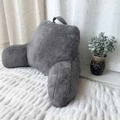 a gray pillow sitting on top of a bed next to a potted plant and window