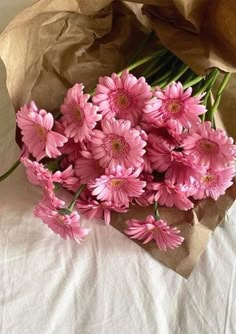 a bunch of pink flowers sitting on top of a white table cloth next to a brown paper bag