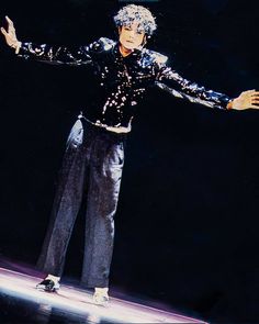 a man in black shirt and pants standing on stage with his arms spread out to the side