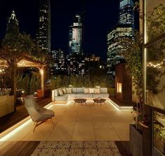 an outdoor living area with couches, tables and lights in the city at night