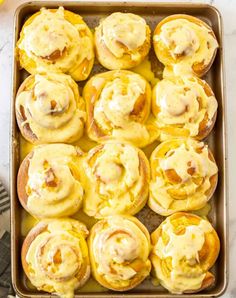 a pan filled with orange rolls covered in icing next to sliced oranges and an orange wedge