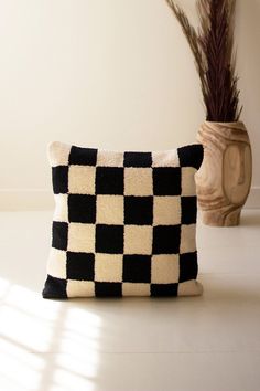 a black and white checkered pillow sitting next to a vase with a plant in it