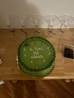 a green cake sitting on top of a wooden table next to wine glasses and condiments