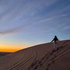 a person riding a snowboard on top of a sand dune at sunset in the desert