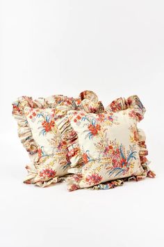 three pillows with ruffled edges and floral print on the front, one in white