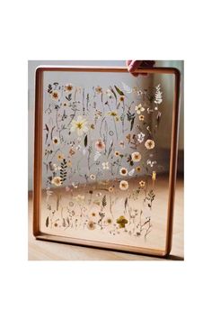 a wooden frame with pressed flowers on the front and bottom, held up by a person's hand