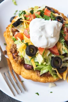 a white plate topped with an enchilada covered in sour cream and black olives