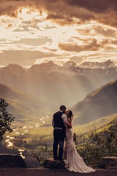 a bride and groom standing on top of a mountain looking out at the valley below