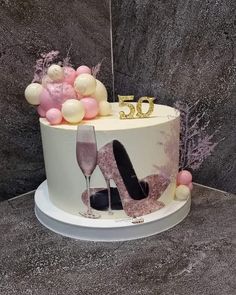 a 50th cake decorated with pink and white balloons, high heel shoes and champagne flutes