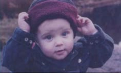 a young boy wearing a hat while standing on top of a rocky hill with his hands behind his head