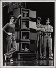 three people standing next to each other in front of a stack of books and boxes