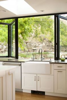 an open kitchen with white cabinets and black glass windows looking out onto the trees outside