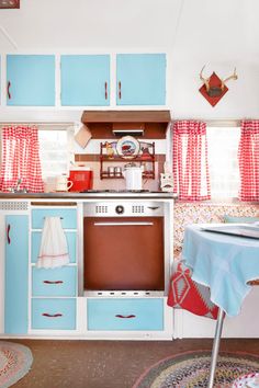 an old fashioned kitchen with blue cabinets and red curtains on the window sill above the stove