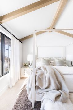 a white bed sitting next to a window in a bedroom under a wooden beam with two lamps on either side